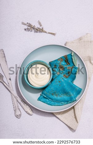 Thin blue pancakes with creamy sauce. Healthy vegan non lactose and gluten free food, breakfast concept. Trendy hard light, dark shadow, light stone concrete background, top view