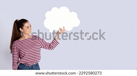Cheerful pretty hispanic young woman in casual outfit holding white conversation bubble on grey studio background, blank free space for design, communication concept, panorama