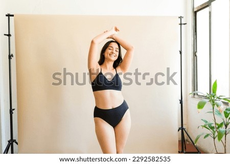 Smiling plus size woman in black underwear with her arms above her head feeling a lot of self love embracing body positivity Royalty-Free Stock Photo #2292582535