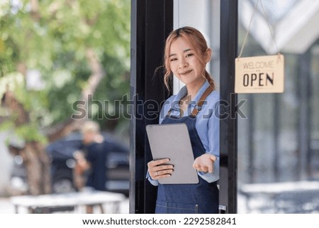 Portrait of Asian attractive small business owner standing in her shop entrance open sign, Portrait of asian tan woman barista cafe owner. SME entrepreneur seller business concept
