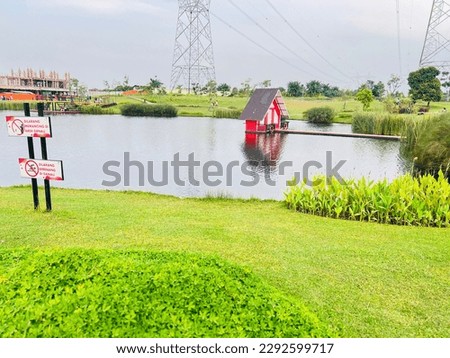 A small lake with small house in the middle surround by the green plant and grass