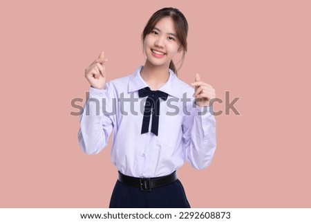 Portrait lovely Asian student girl in Thai school uniform showing mini heart hand sign isolated on pink background.