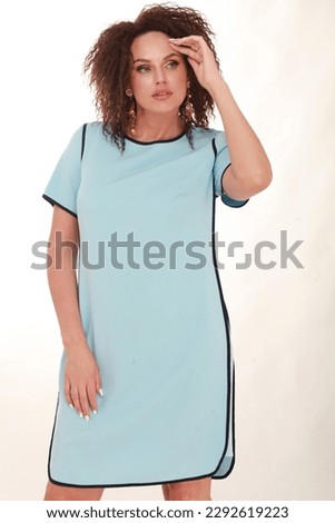 Beautiful middle aged plus size woman posing in studio. Female with afro hairstyle, makeup dressed in blue summer dress and heels. Catalog fashion shooting for new spring summer season
