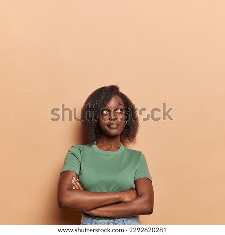 Vertical shot of thougthful dark skinned woman student with short hair plans actions after university concentrated above dressed in casual t shirt isolated over brown wall tries to remember something