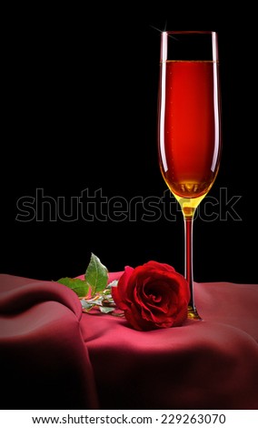 glass of champagne and red rose on black background