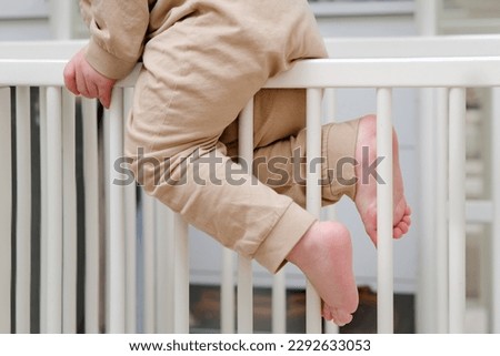 Baby escapes from the crib by climbing over the bars. The child climbs over the bed rail. Kid aged about two years (one year nine months) Royalty-Free Stock Photo #2292633053
