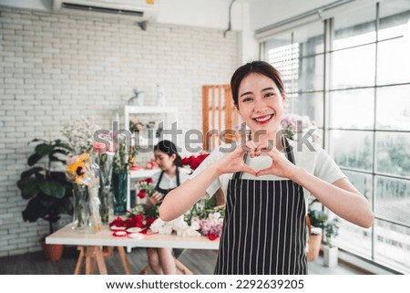 Young female florist taking pictures to promote the shop girls making miniheart hand and bright smiling faces in a flower shop full of flowers.