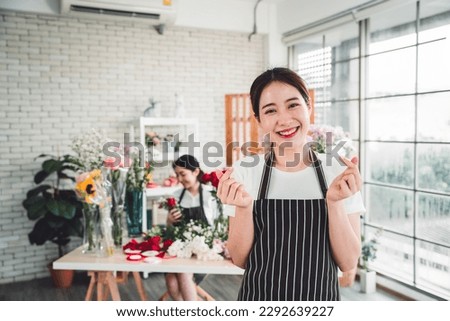 Young female florist taking pictures to promote the shop girls making miniheart hand and bright smiling faces in a flower shop full of flowers.