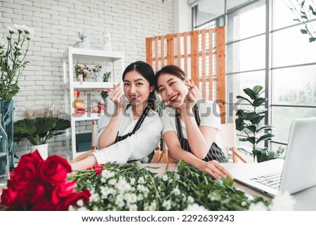 Young female florist taking pictures to promote the shop two girls making miniheart hand and bright smiling faces in a flower shop full of flowers.