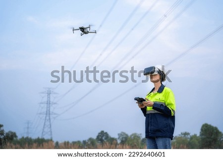 A female electrical engineer wearing vr goggles using drone to inspect power station to explore power poles in aerial view, technology concept and innovation of power generation. Royalty-Free Stock Photo #2292640601