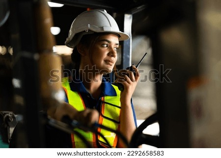 Indian woman worker driving a forklift and using a walkie-talkie at warehouse factory container. communication radio. Inventory and wholesale concept Royalty-Free Stock Photo #2292658583