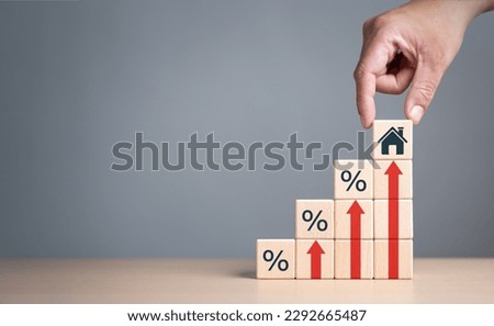 Real estate property investment concept. Asset management, Interest rates, inflation, loan mortgage, increase tax. Hand holding house icon on wooden cube from stack block with percent and rise arrow. Royalty-Free Stock Photo #2292665487