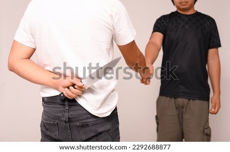 Two male shaking hand with one hand holding a knife on white background.Weak trust. Backstabbing friends.Man hold and hide knife at the back ready to kill.Blackmail and unreliable partnership concept. Royalty-Free Stock Photo #2292688877