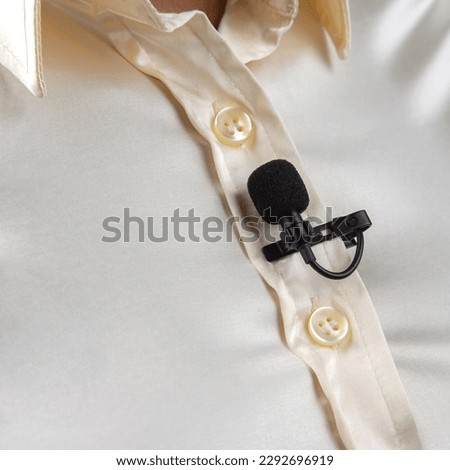 The lavalier microphone is secured with a clip on a women shirt close-up. Audio recording of the sound of the voice on a condenser microphone