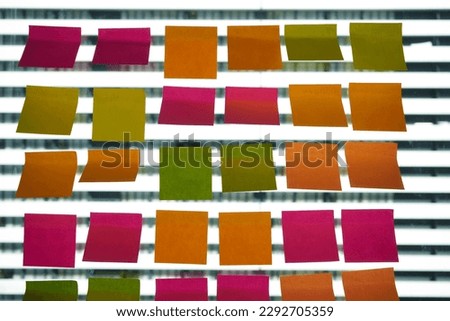 Abstract empty adhesive post it paper on glass wall or window with reflect in startup business office . Colorful reminder paper note and copy space at workplace. Post it paper note