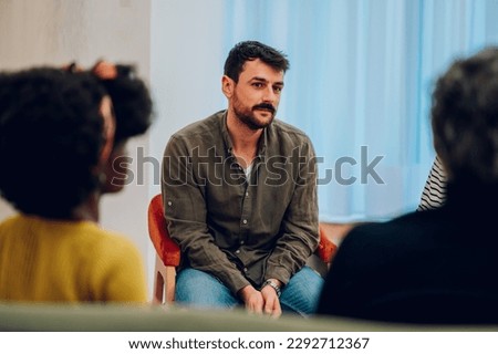 Portrait of a sad young man talking about his problems during a meeting at mental health center. Group therapy participants sitting in a circle and talking. Mental health concept. Copy space. Royalty-Free Stock Photo #2292712367