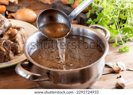 Saucepan with bouillon with a ladle on rustic wooden table. Bone broth