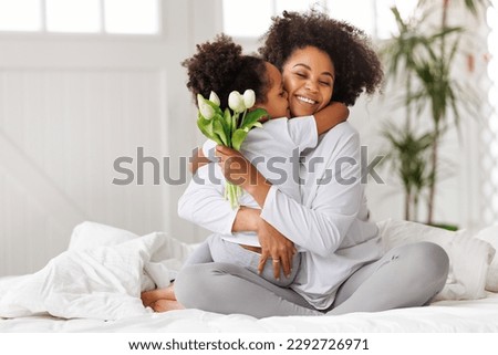 Happy mother's day! american family happy baby daughter congratulates mom on the holiday, hugs her and gives bouquet of flowers at home