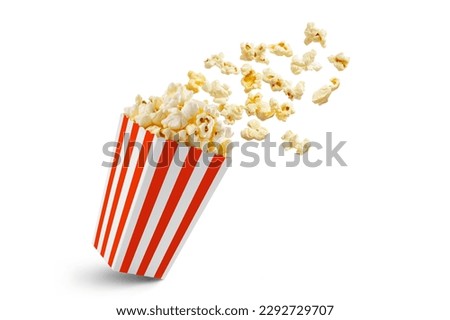 Popcorn flying out of red white striped paper box isolated on white background with copy space. Splash, levitation of popcorn grains.  Royalty-Free Stock Photo #2292729707