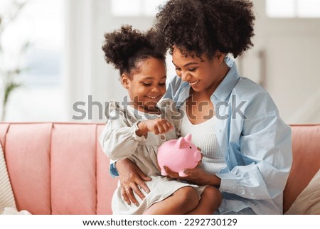financial education. african american family, mother and child daughter with pig piggy bank counting savings at home on sofa
