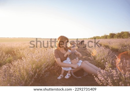 Portrait of brunette mother with little daughter sitting in purple lavender field. Young woman in rural dress lovingly embraces, kisses girl. The concept of allergy, travel, single parent. Copy space