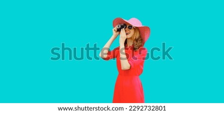 Summer portrait of happy smiling young woman photographer with film camera wearing straw hat, pink dress, sunglasses on blue background