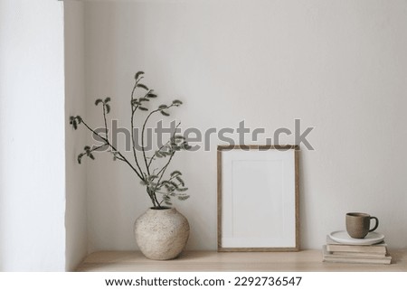 Breakfast still life. Modern living room. Cup of coffee, books. Empty wooden picture frame mockup on desk, table. Vase with green willow tree branches. Elegant Scandi working space, home office. 