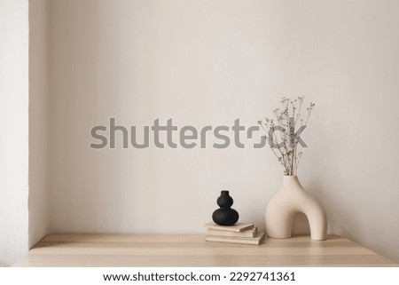 Artistic interior still life. Modern organic, geometric shaped sculptures. Vase with dry flowers, grass and old books on wooden table. Home staging, minimal decor concept. Empty beige wall background.