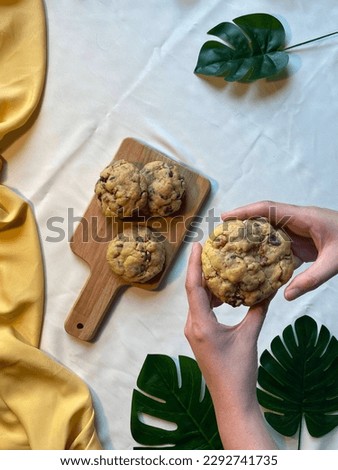 Chocolate Chip Cookies with nut, on a wooden tray, wooden board, leafs in the corner, hands in the picture, hand holding cookies, breaking cookies, break a part, tropical vibes