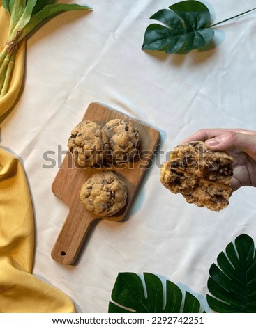 Chocolate Chip Cookies with nut, on a wooden tray, wooden board, leafs in the corner, hands in the picture, hand holding cookies, breaking cookies, break a part, tropical vibes