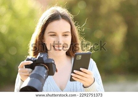 Happy photographer checking phone holding mirrorless camera in a park