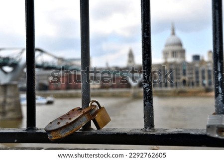 A magnificent and antiquated padlock affixed to a railing, with a hazy view of the iconic St Paul's cathedral and the illustrious Millenium bridge in the background