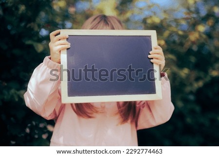 
Unrecognizable Child Holding a Blackboard Announcement Placard. Preschool kid showing a blank empty sign for copy space
