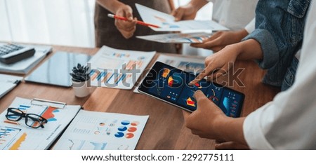 Analyst team utilizing BI Fintech to analyze financial report with tablet over paper on table and analyzing BI power dashboard display on tablet screen for business insight. Panorama shot. Scrutinize Royalty-Free Stock Photo #2292775111