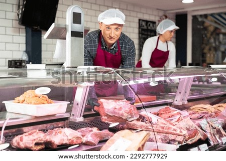Smiling male butcher offering to sell big piece of beef in butcher shop Royalty-Free Stock Photo #2292777929