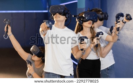 in computer club, group of four friends wearing virtual reality glasses and with joysticks are playing dynamic game with modern graphics. Royalty-Free Stock Photo #2292778025