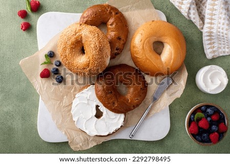 Homemade freshly baked bagels on a parchment paper ready to eat, cinnamon raisin, sesame and plain bagel served with cream cheese and fresh berries Royalty-Free Stock Photo #2292798495
