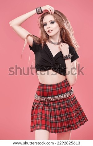 Glamorous teenage girl with dark smoky makeup and rock-style hair styling poses against a pink studio background. Youth fashion and lifestyle. Youth pop and rock culture. 