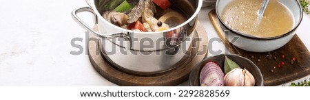 Beef broth of beef meat on bones slow cooked with vegetables: carrot, onion, garlic, and spices served in a pot on a white background with ingredients, top view. Panorama with copy space.
