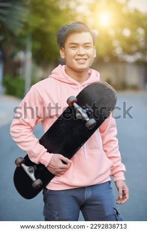 Portrait of smiling young man holding his skateboard and smiling at camera