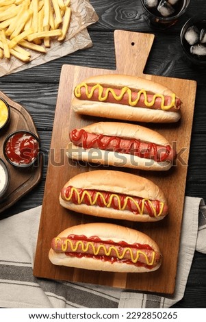 Delicious hot dogs with mustard, ketchup and potato fries on black wooden table, flat lay Royalty-Free Stock Photo #2292850265