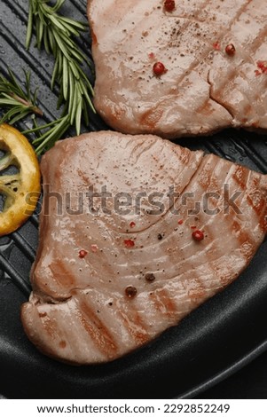Delicious tuna steaks, lemon and rosemary in grill pan, top view