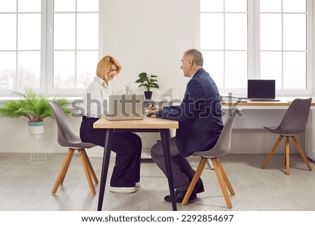 Two people meeting in office. Smiling financial consultant, loan broker or business advisor makes her client sign contract agreement. Side view of young woman and senior man sitting at table Royalty-Free Stock Photo #2292854697