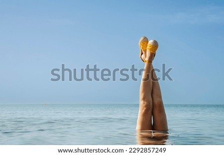 Photo of a woman's legs in yellow sandals in a serene body of water.
