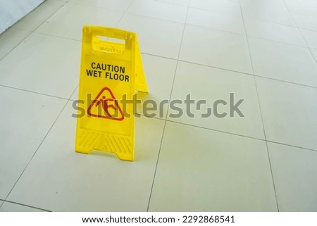 Yellow caution sign saying wet floor prevent people from falling on surface. Warning of slippery area for client or customer safety. Housekeeping, janitor concept. Maintenance and cleanup.