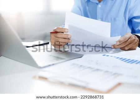 Asian businessman reviewing document reports at office workplace with computer laptop. legal expert, professional lawyer reading and checking financial documents with chart or insurance contract