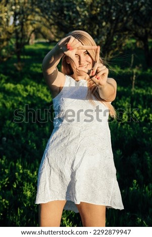 a woman in a white dress in a blooming garden in a park in nature journey walking shows a square with her fingers