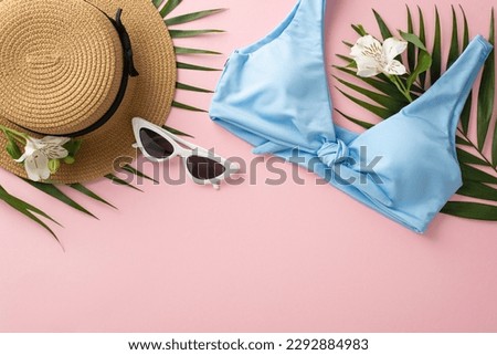 Get ready for summer! Top view flat lay of blue swimsuit with sunhat, green palm leaves, sunglasses, and flowers on pastel pink background with empty space for text or advert