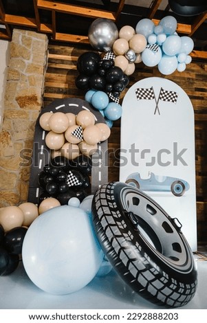 Trendy decor with flag, race, wheel, car for boy. Birthday decorations with blue, brown, black, silver balloons for party. Arch for a celebration event. Photo wall decoration space or place for text.