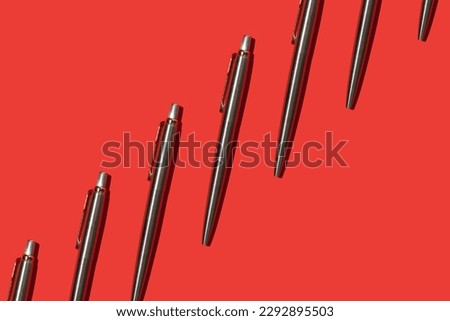 metal ballpoint pens on red background pattern Royalty-Free Stock Photo #2292895503